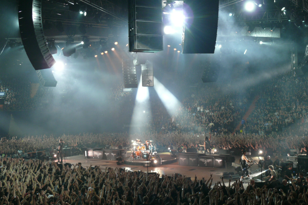 Metallica plays while surrounded by an audience huge speakers hang above the crowd